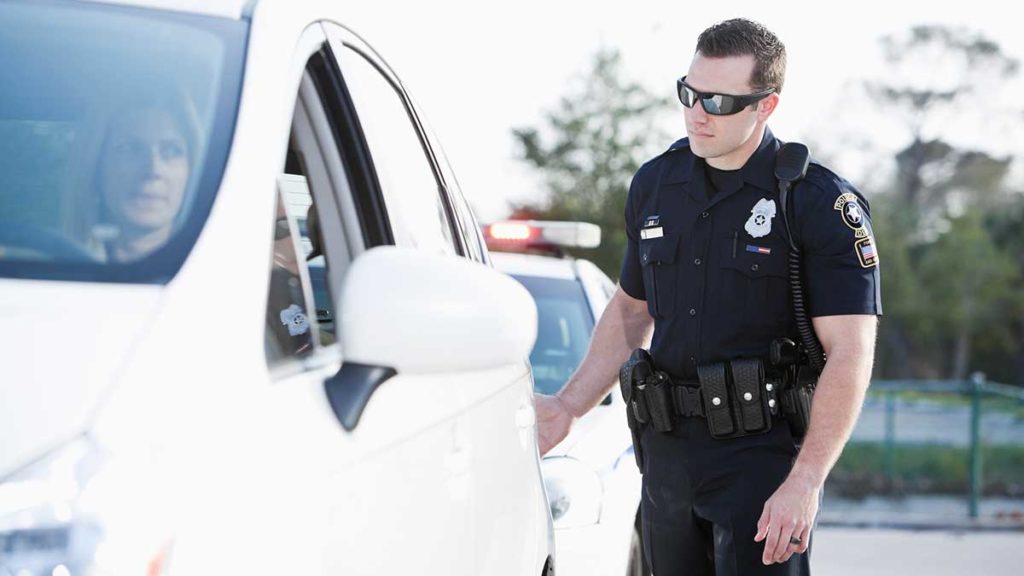 Woman in a white vehicle being pulled over by a police officer. She may need bad driving record insurance. 