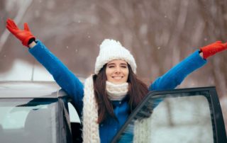 Woman dressed for winter with armed raised looking happy with car