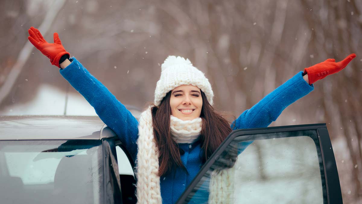 Woman dressed for winter with armed raised looking happy with car