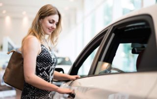 Woman is in a dealership buying a new car - opening a floor model car door.