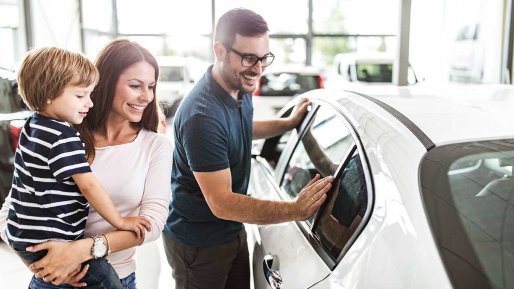 Happy couple with child buying a used car - shopping in a dealership