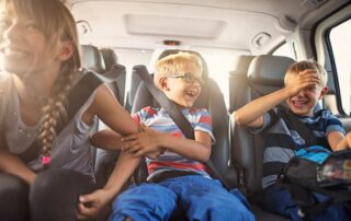 3 kids in back seat of car laughing - car activities for kids on road trips