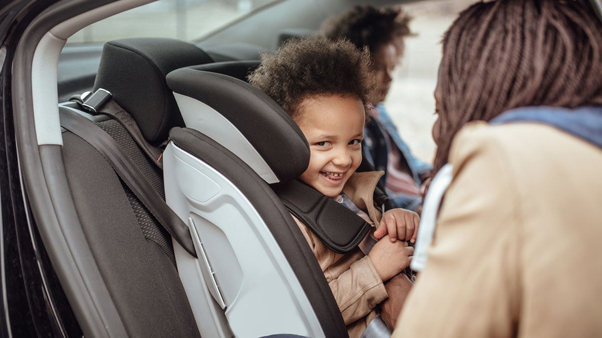 Close up of a mother buckling her younger daughter into car seat