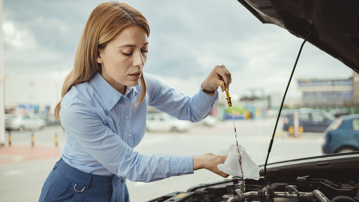 Woman driver checking level of oil on a car engine dipstick