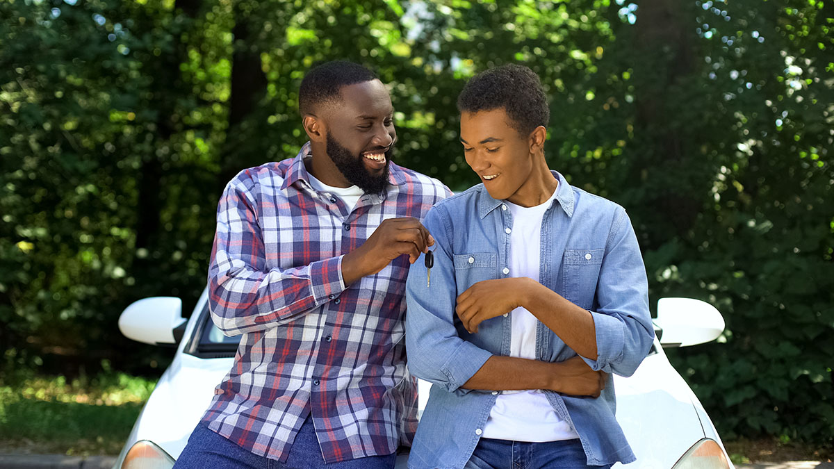 Happy dad giving car key to teenage son, permission to drive, parenthood trust, family