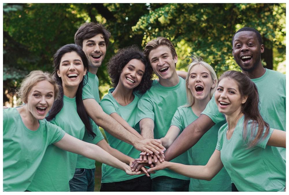 Team of smiling young people in matching green shirts with their hands joined together.