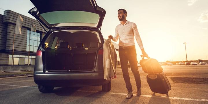 Man with luggage next to a car with an open trunk