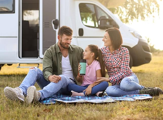 Family sitting on grass outside motor home - link to The General Labs RV Insurance page